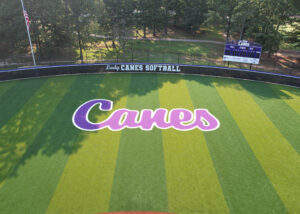 Clean, low-altitude aerial featuring the purp Lady Canes wordmark and striped outfield pattern