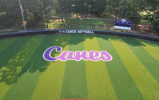 Clean, low-altitude aerial featuring the purp Lady Canes wordmark and striped outfield pattern